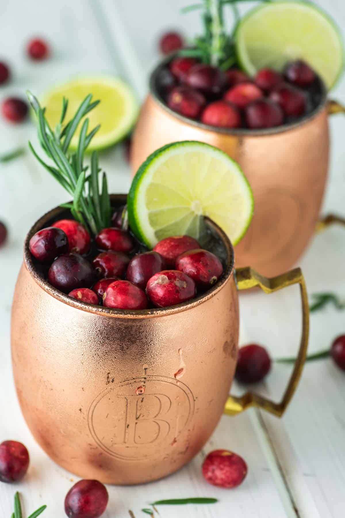 Cranberry Moscow Mule cocktails served in copper mule mugs and garnished with lime slices, rosemary sprigs, and fresh cranberries