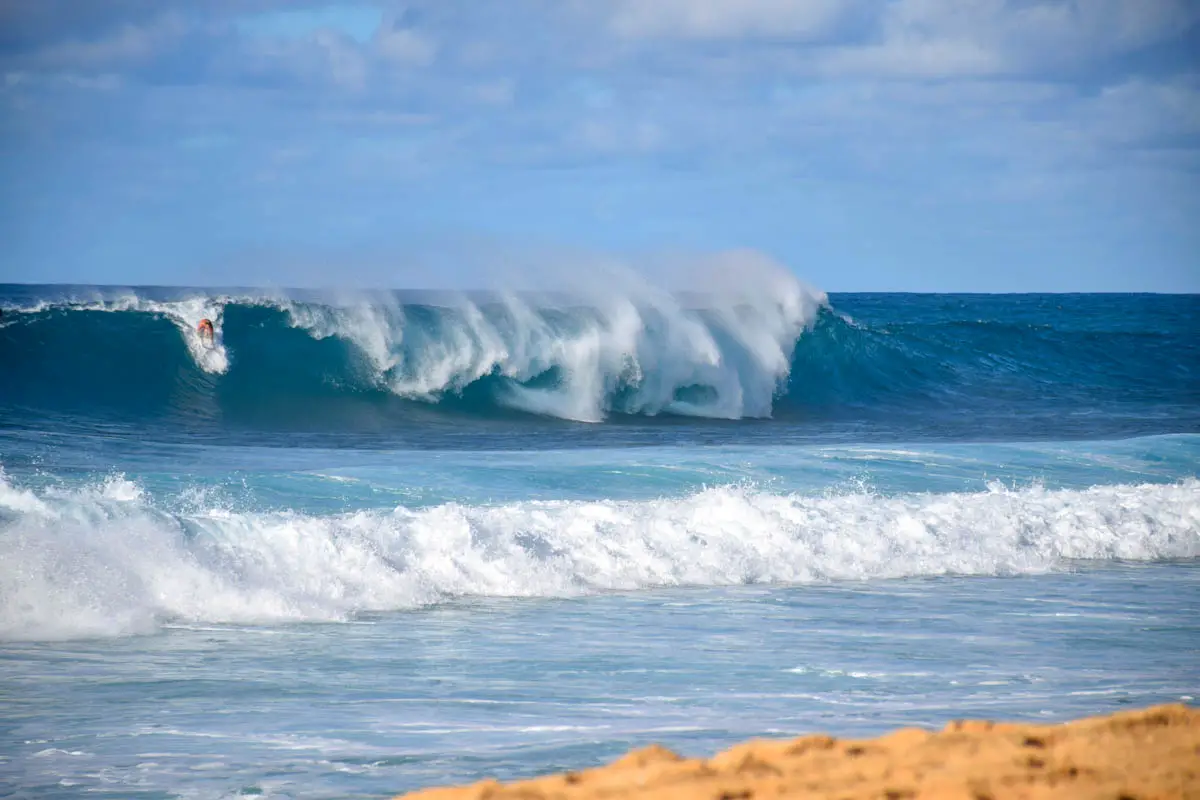 Surfer rides a rainbow wave at the Banzai Pipeline at Ehukai Beach on Oahu in Hawaii