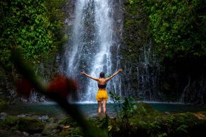Woman raises hands in front of a waterfall in Costa Rica