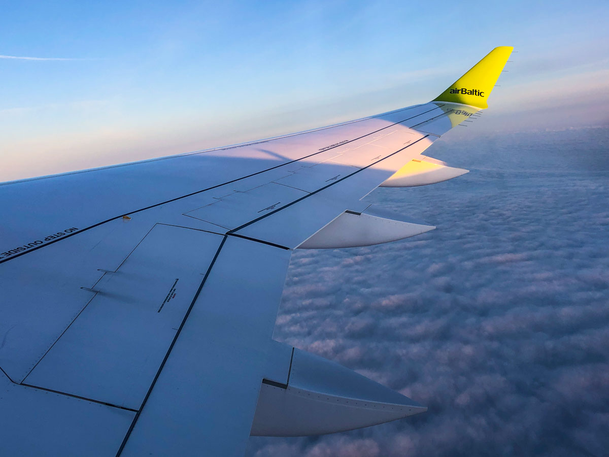 View out the plane window of an Air Baltic airplane wing above the clouds on a morning flight from Riga, Latvia, to Amsterdam