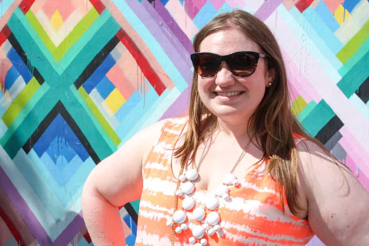 Female traveler wears designer Oliver Peoples sunglasses in front of a mural at Wynwood Walls in Miami, Florida 