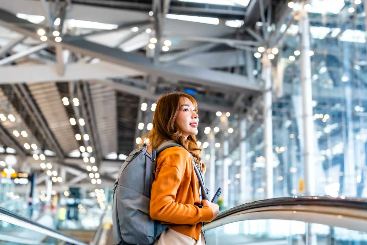Female student wearing a backpack rides escalator in an international airport