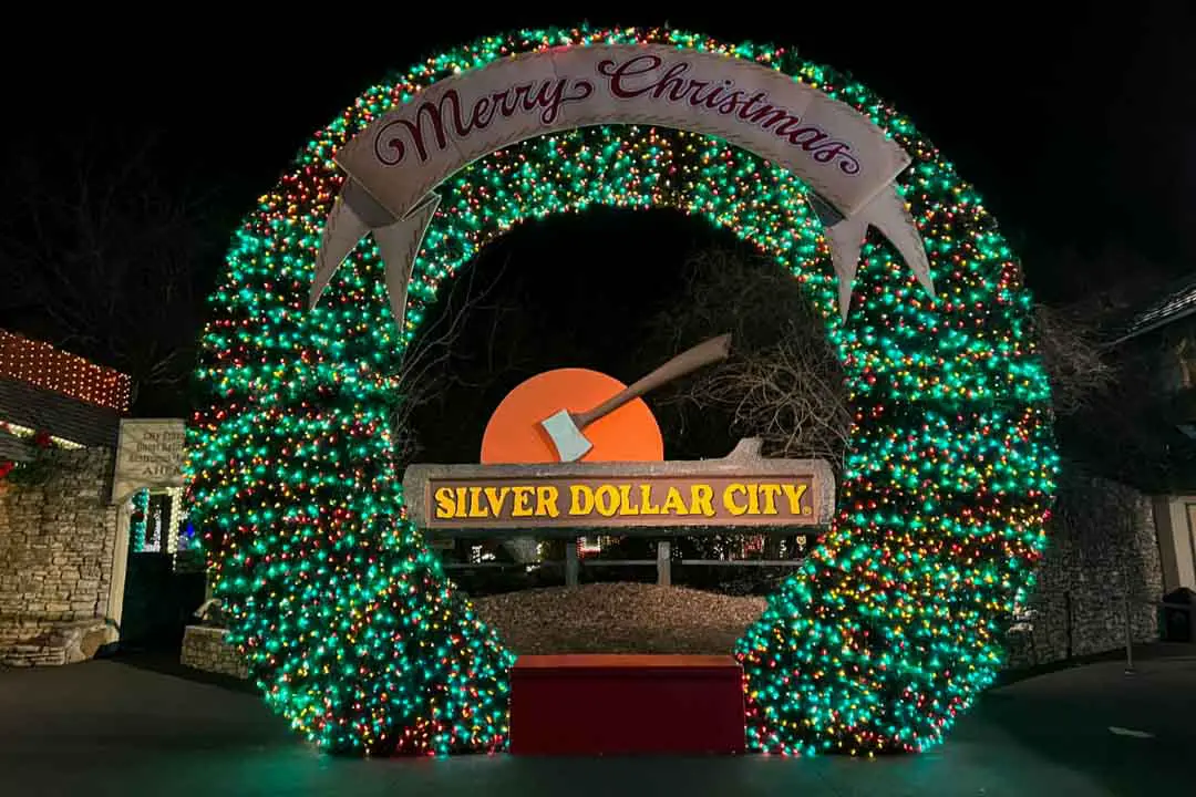 A large holiday wreath decorated with twinkling lights frames the Silver Dollar City sign at the entrance to Silver Dollar City theme park in Branson, Missouri, during the Christmas holiday season