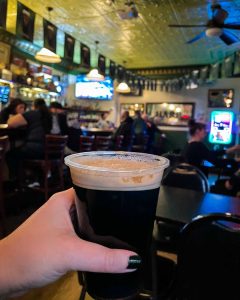 A pint of Guinness in a plastic cup is held in a woman's hand at Nancy Whiskey's, an Irish bar in Detroit's Corktown neighborhood