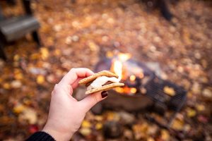 S'more held in a woman's hand with campfire in the background
