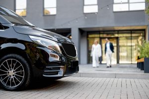 A man and a woman walk to a black shuttle service vehicle