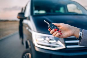 Woman's hand holds a vehicle key with the vehicle in the background