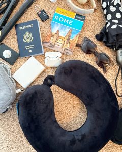 Europe travel essentials including a Brookstone travel neck pillow, AirTag, power bank, Airpods, sunglasses, umbrella, tech organizer, passport, and pocket guidebook