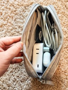 Travel tech organizer case holding Europe plug adapter, earbuds case, power bank, AirTag, and various charger cords