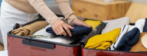 Close-up image of a woman's hands packing clothing into a red suitcase