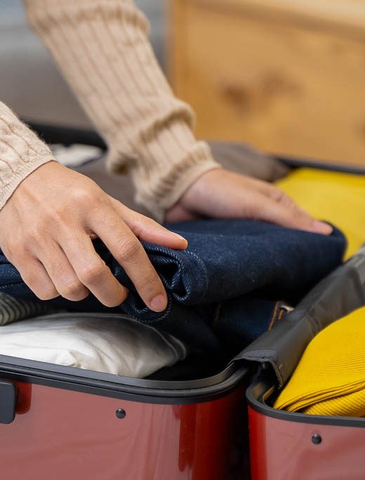 Close-up image of a woman's hands packing clothing into a red suitcase